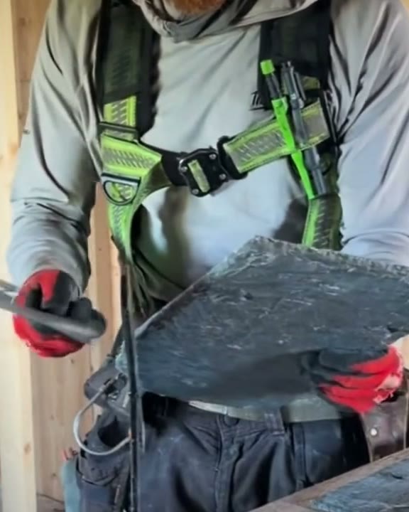 One of our roofers, in a harness, trimming a slate by hand